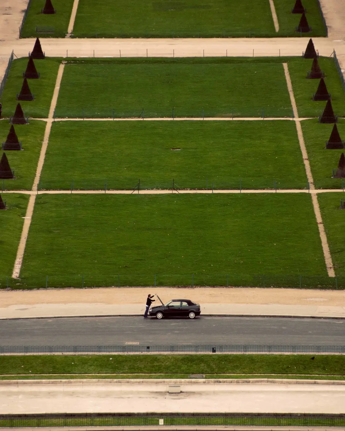 A single car on a road beside a park laid out in a ruled grid of lawns