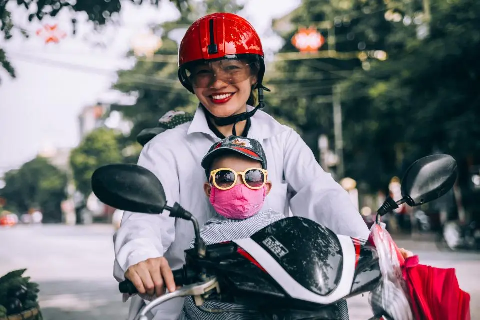 A mother and her son riding a scooter, both in helmets