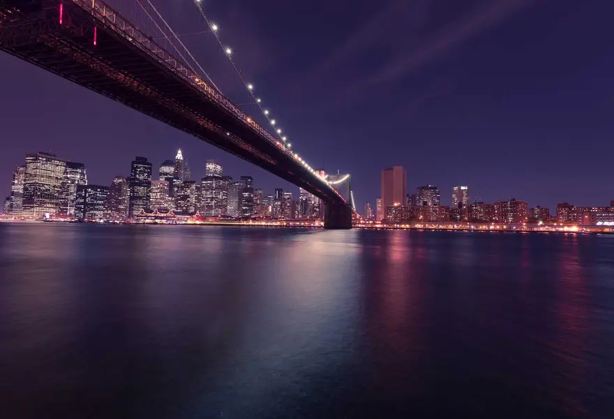A long suspension bridge leading to a city skyline at night